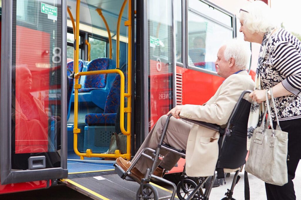 Une personne âgée qui en aide une autre en fauteuil roulant à remonter la rampe d'un autobus